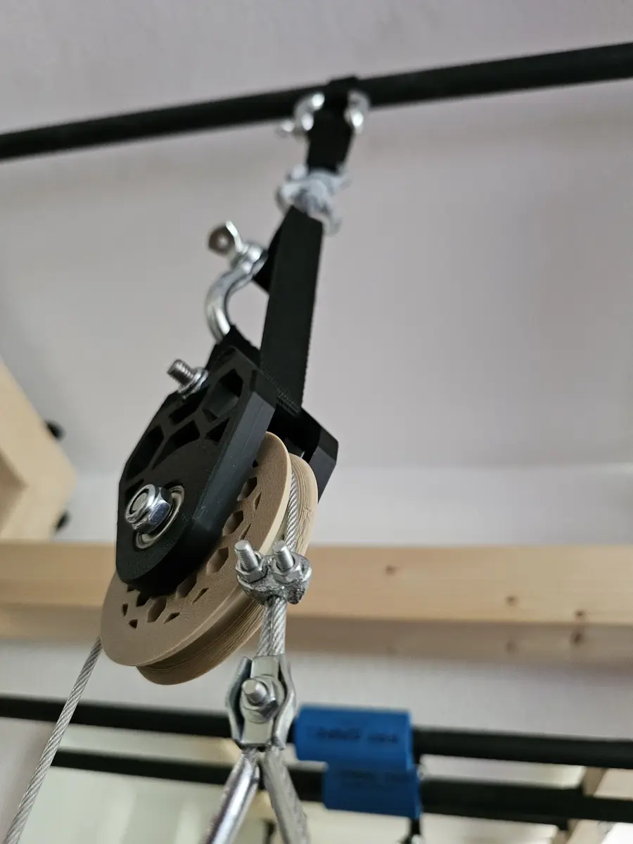 Gedruckte Umlenkrolle mit Gurt, Schäkel und Stahlseil an einer Stange unter der Decke