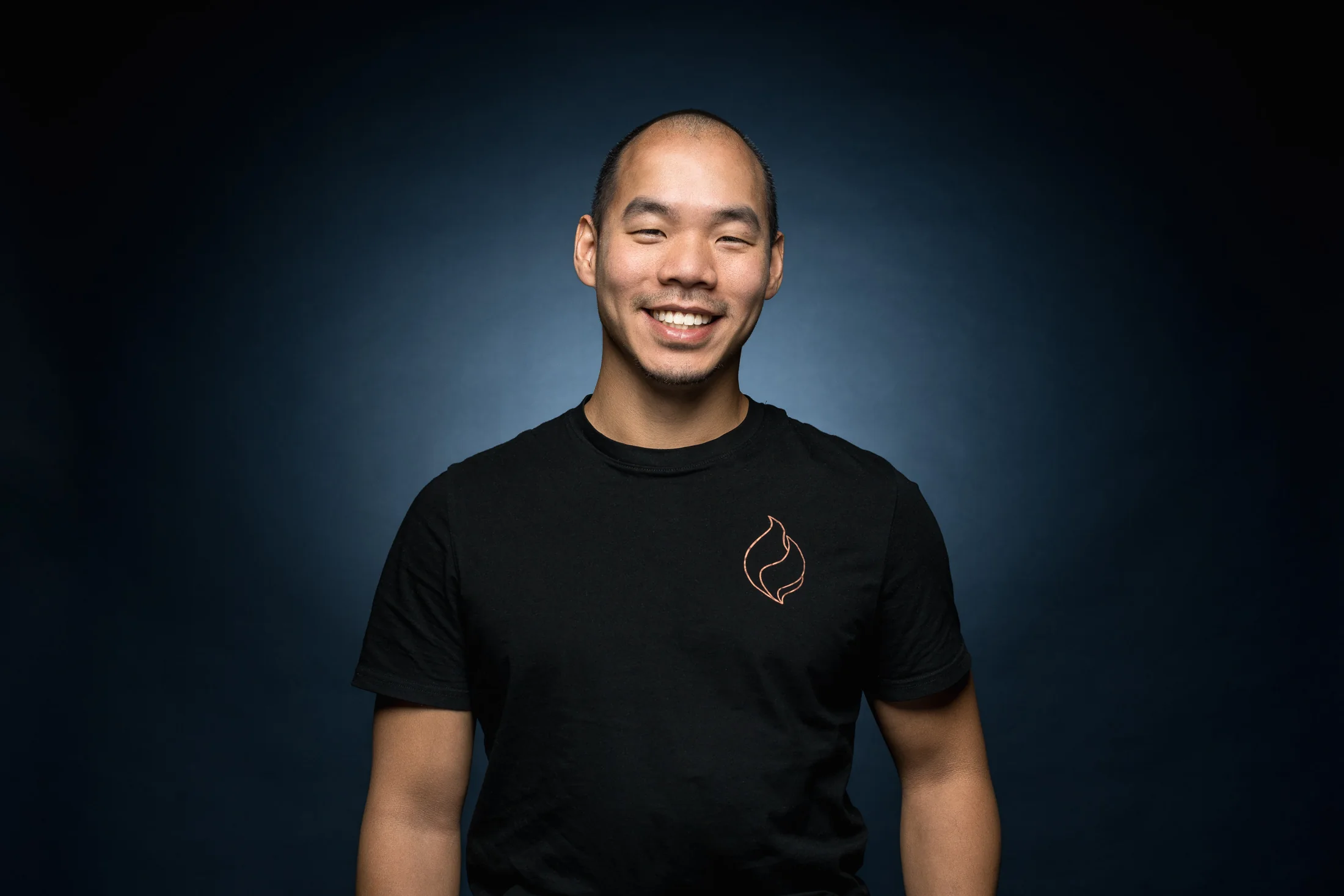Thanh Nguyen lächelnd im schwarzen Bachata-Viersen-Shirt vor dunkelblauem Hintergrund